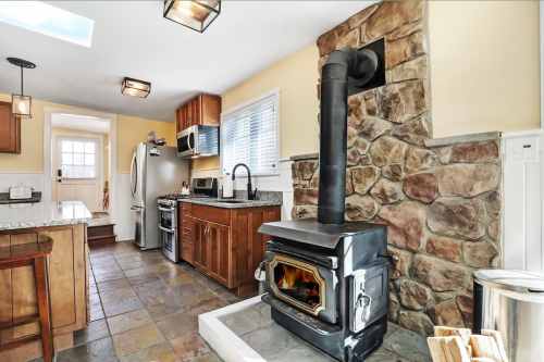Cozy kitchen featuring a stone wall, wood stove, modern appliances, and warm lighting.
