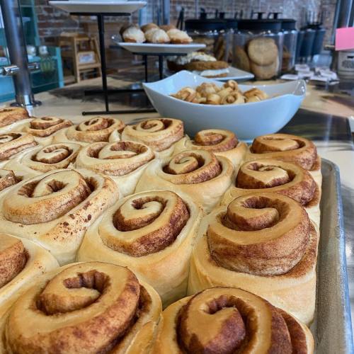 A tray of freshly baked cinnamon rolls with a background of assorted pastries on display.