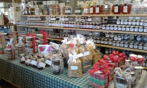 A display of various jars and packages of jams, candies, and snacks on a table with a checkered tablecloth.