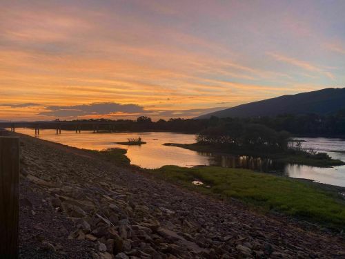 A serene river at sunset, with colorful skies reflecting on the water and mountains in the background.