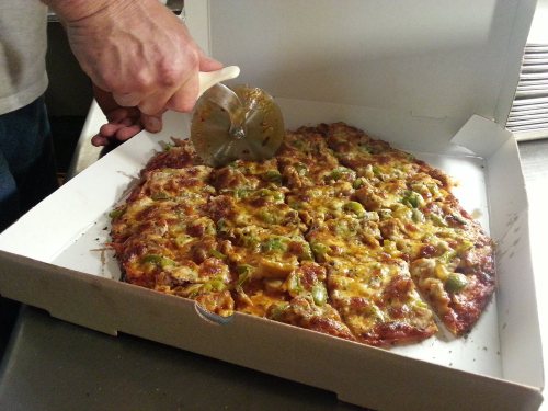 A person using a pizza cutter to slice a freshly baked pizza in a takeout box.