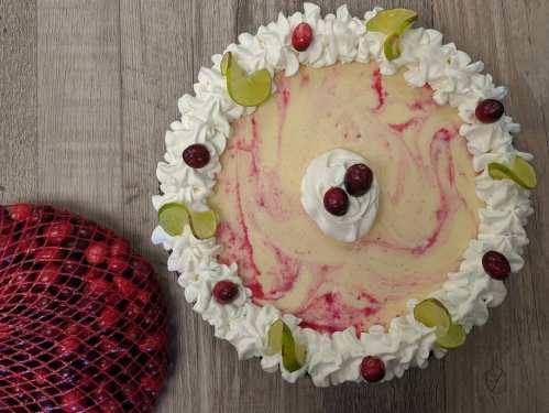 A creamy dessert topped with whipped cream, cranberries, and green grapes, beside a bag of fresh cranberries.