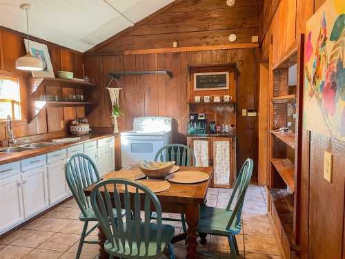 Cozy kitchen with wooden walls, a dining table, and a white stove, featuring green chairs and rustic decor.