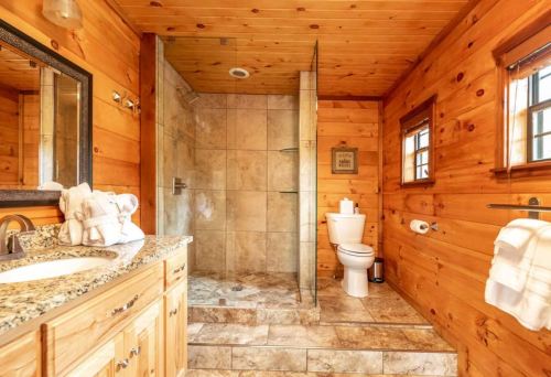 Cozy wooden bathroom featuring a glass shower, toilet, sink with granite countertop, and rustic decor.