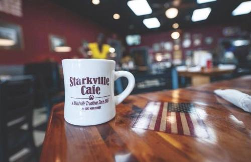 A white coffee mug with "Starkville Cafe" printed on it, placed on a wooden table with an American flag design.