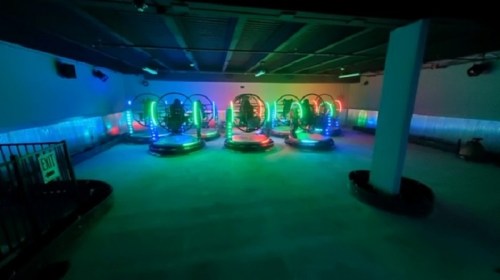 A dimly lit indoor amusement area with colorful, illuminated bumper cars in a circular arrangement.