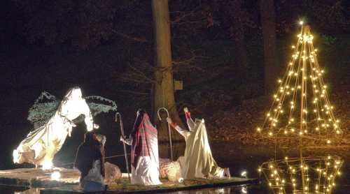 A serene night scene featuring a lit Christmas tree and figures in robes on a raft, reflecting in the water.