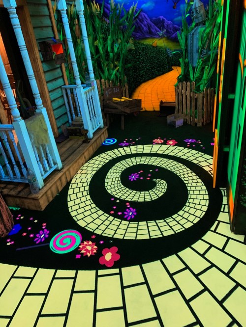 A colorful spiral pathway with flowers and lollipops, leading from a whimsical house to a vibrant, green landscape.