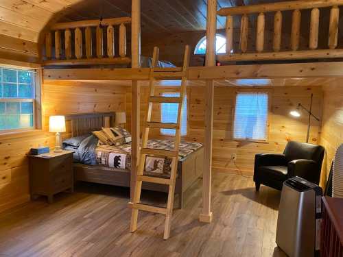 Cozy wooden cabin interior with a lofted bed, ladder, and seating area, featuring warm lighting and natural wood finishes.
