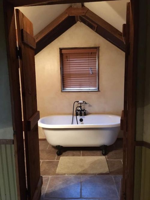 A cozy bathroom featuring a freestanding bathtub under a sloped ceiling, with wooden doors and a window with blinds.