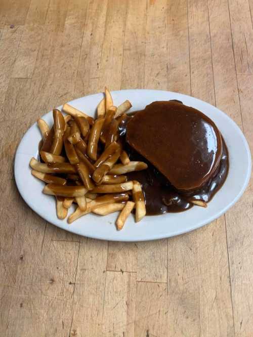 A plate of fries and a hamburger smothered in brown gravy on a wooden table.