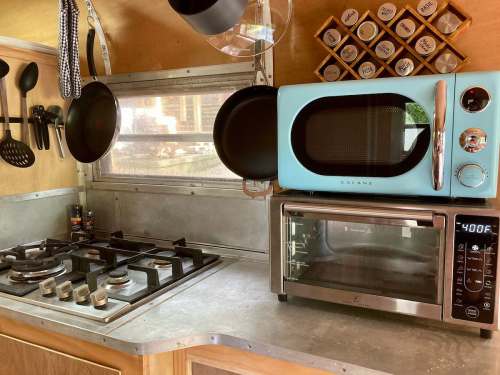 A compact kitchen with a blue microwave, stainless steel oven, and cooking utensils hanging on the wall.