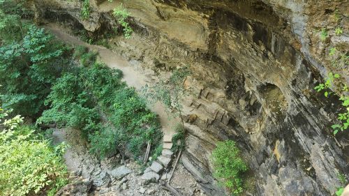 A rocky cliffside with a winding path surrounded by lush greenery and trees.