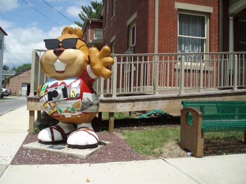 A large, cartoonish beaver statue wearing sunglasses and a red shirt, standing outside a brick building.