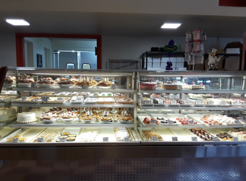 A display case filled with various desserts, including cakes, pastries, and sweets, in a bright bakery setting.