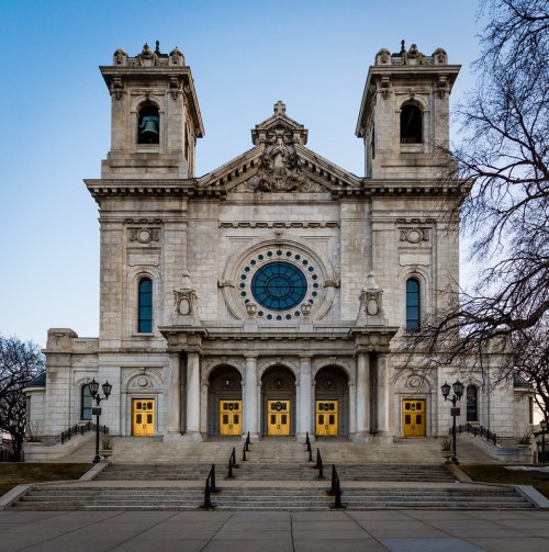 Historic building with ornate architecture, featuring a large circular window and golden doors, set against a clear blue sky.