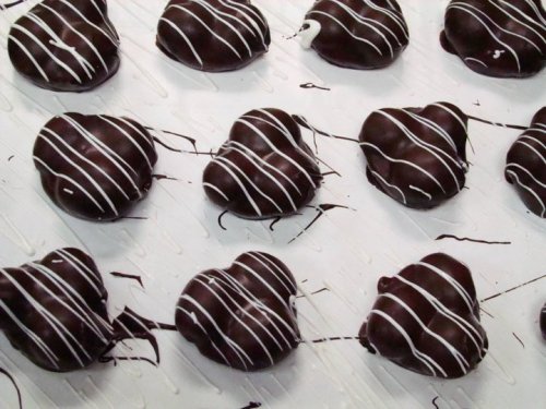 A close-up of heart-shaped chocolate treats drizzled with white chocolate on a white surface.