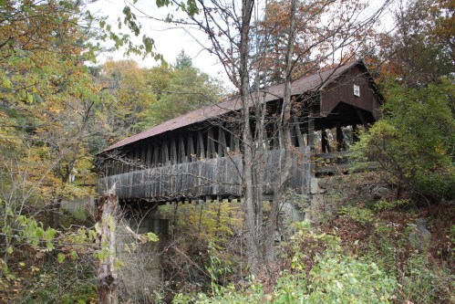 A rustic covered bridge surrounded by trees and autumn foliage, spanning a small creek.