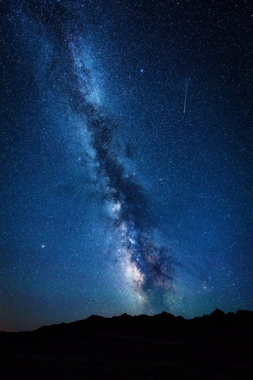 A stunning view of the Milky Way galaxy filled with stars, set against a dark night sky and silhouetted mountains below.