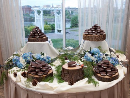 A dessert display featuring stacked chocolate cookies on wooden stands, surrounded by blue flowers and pinecones.