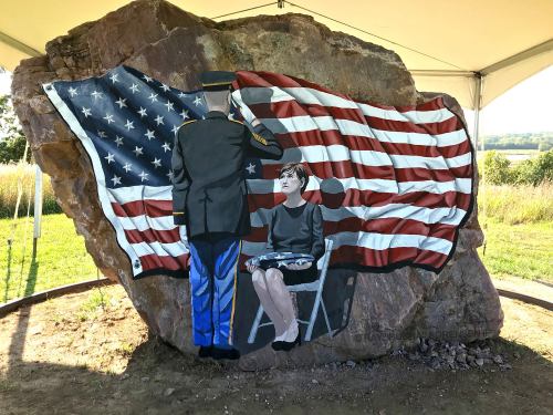 A mural on a rock depicts a soldier saluting a seated woman in front of a large American flag.
