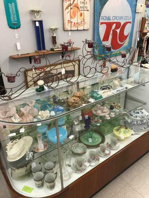 A display case filled with vintage glassware, ceramics, and decorative items in a quaint shop setting.