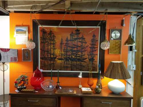 A display of vintage decor featuring a ship painting, lamps, and various decorative items against an orange wall.