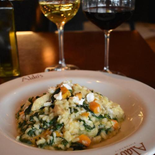A plate of creamy risotto with spinach and feta, accompanied by glasses of white and red wine.