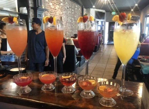 A variety of colorful cocktails in tall glasses, garnished with fruit, displayed on a bar counter.