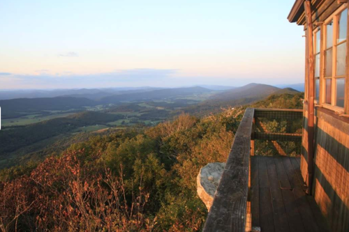 A scenic view from a wooden lookout tower, overlooking rolling hills and valleys at sunset.