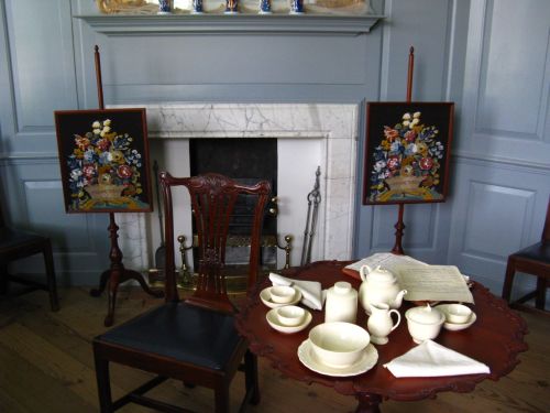 A vintage room with a wooden table set for tea, featuring a teapot, cups, and decorative paintings on easels.