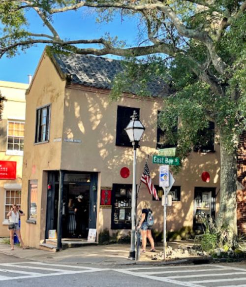 Historic building on a corner with a street sign for East Bay, featuring shutters and a lamppost, surrounded by trees.