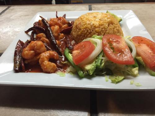 A plate of shrimp in a spicy sauce, served with yellow rice, lettuce, tomato, and green pepper slices.