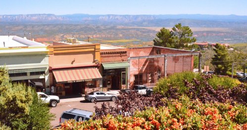 Scenic view of a small town with shops, parked cars, and mountains in the background under a clear blue sky.