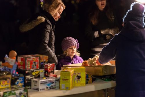 A child in a purple hat smiles at a table filled with toys, while adults engage in conversation nearby.