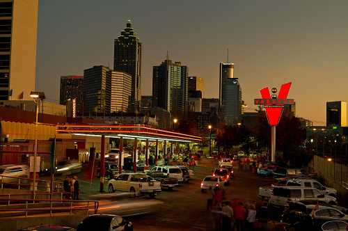 A vibrant cityscape of Atlanta at dusk, featuring a retro diner and bustling streets filled with cars and people.