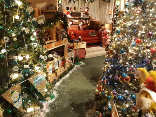A cozy holiday scene with decorated Christmas trees, festive decorations, and a red couch in a warmly lit room.