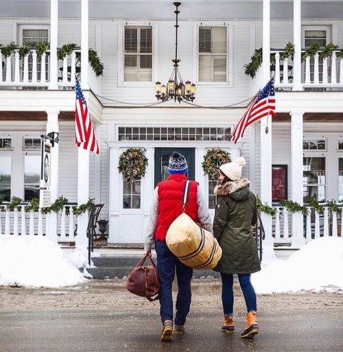 A couple walks towards a charming, decorated building with American flags and snow-covered ground.