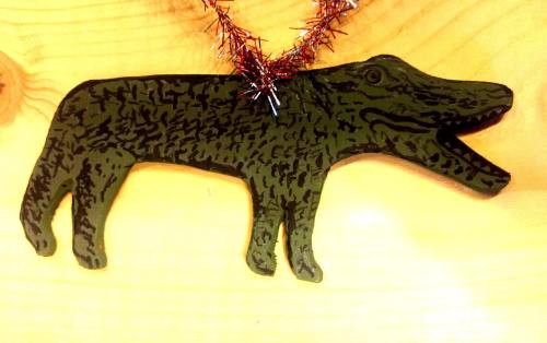 A wooden decoration shaped like a crocodile, featuring a textured green surface and a festive tinsel necklace.