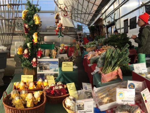 A vibrant market stall filled with fresh produce, festive decorations, and various local goods in a greenhouse setting.