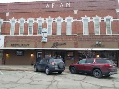 Exterior of a brick building featuring a restaurant and lounge, with parked cars in front.