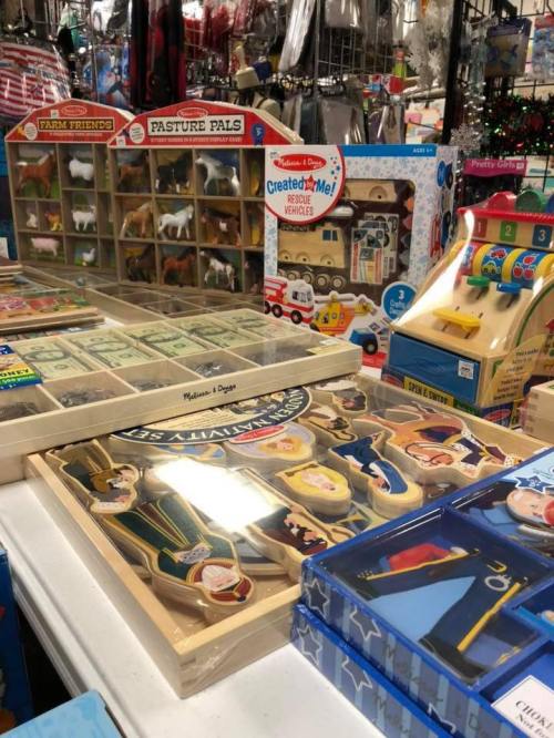 A colorful display of children's toys, including puzzles, figurines, and playsets, on a table in a store.
