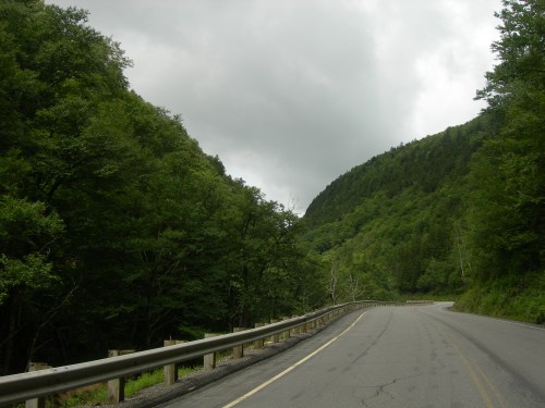 A winding road surrounded by lush green trees and hills under a cloudy sky.