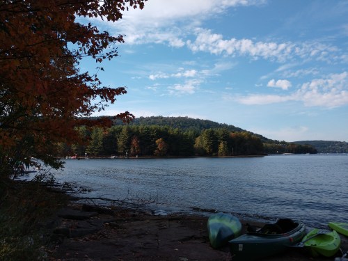 A serene lake scene with colorful autumn trees, a clear sky, and kayaks on the shore.