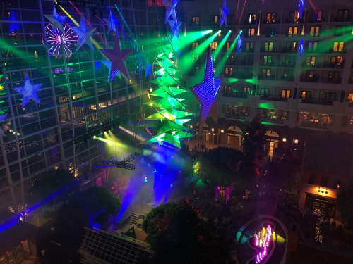 Colorful lights and stars illuminate a festive indoor space, featuring a large decorated tree and vibrant displays.