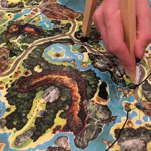 A hand holding a pencil points to a detailed map featuring islands, rivers, and a volcano.