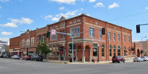Historic brick building at a street corner, featuring arched windows and decorative details, under a blue sky.