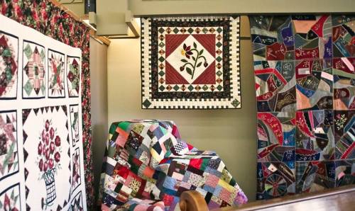 A display of colorful quilts hanging on walls, showcasing various patterns and designs in a cozy setting.