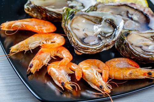 A black plate featuring fresh oysters and several cooked shrimp, showcasing a seafood delicacy.