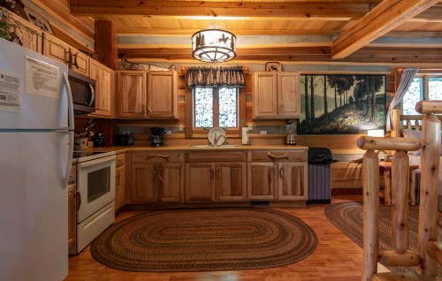 Cozy wooden kitchen with modern appliances, a round rug, and a scenic painting on the wall. Warm, inviting atmosphere.